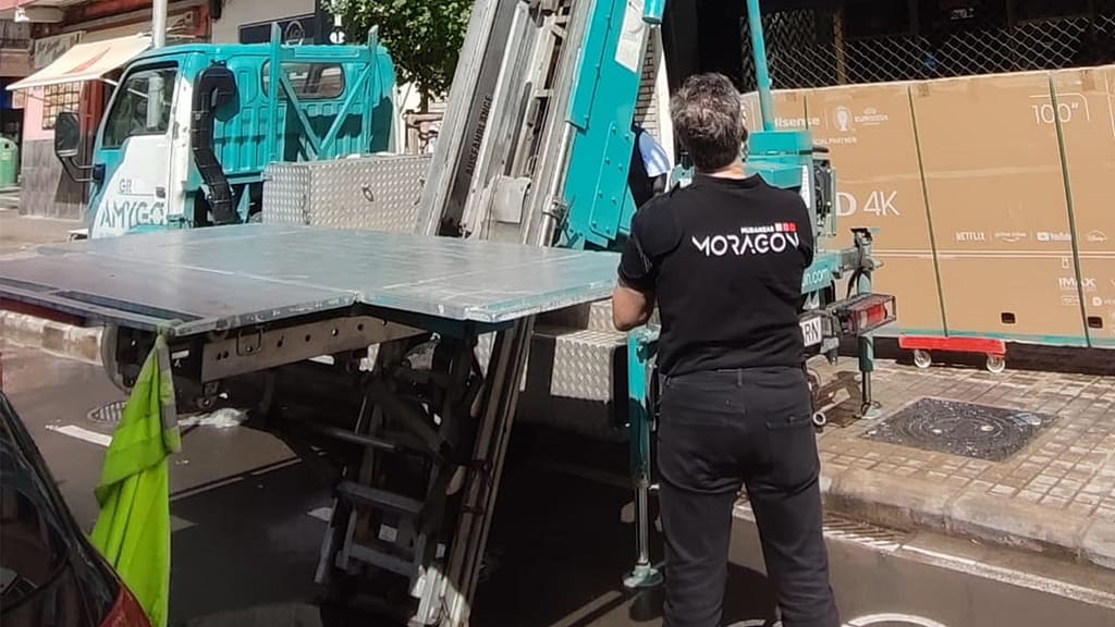 Operario de Mudanzas Moragon manejando plataforma elevadora para subir un televisor de grandes dimensiones en la calle.